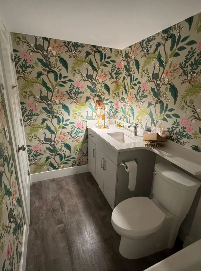 Bathroom interior with floral print walls, toilet, sink, and shower.