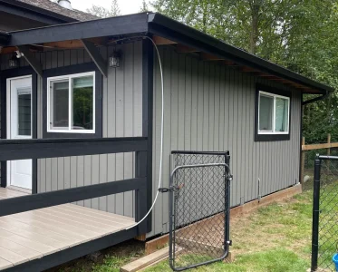 Small gray house with black door and fence in a yard.