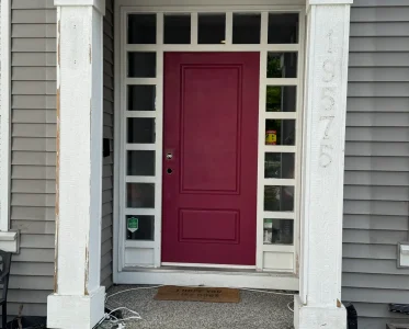 Open red front door with white trim, inviting entry to a white house.