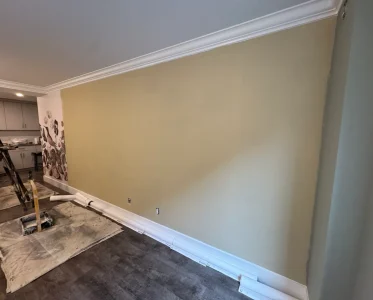 A large, empty room with a light yellow wall and white baseboard under construction.