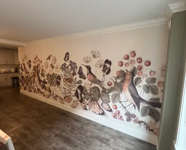 Vibrant mural of birds and fruits on a room wall, with a couch in the background.