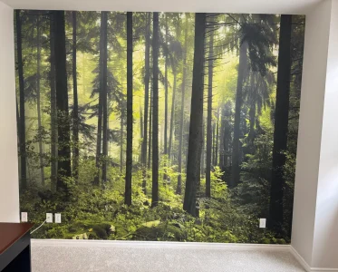 Mural of a lush green forest on a room wall, with a couch and chair inside.