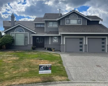 A large two-story gray house with a garage on a well-manicured lawn.