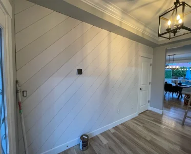 A dining room under construction with a white wall, doorway, paint bucket, and hammer.